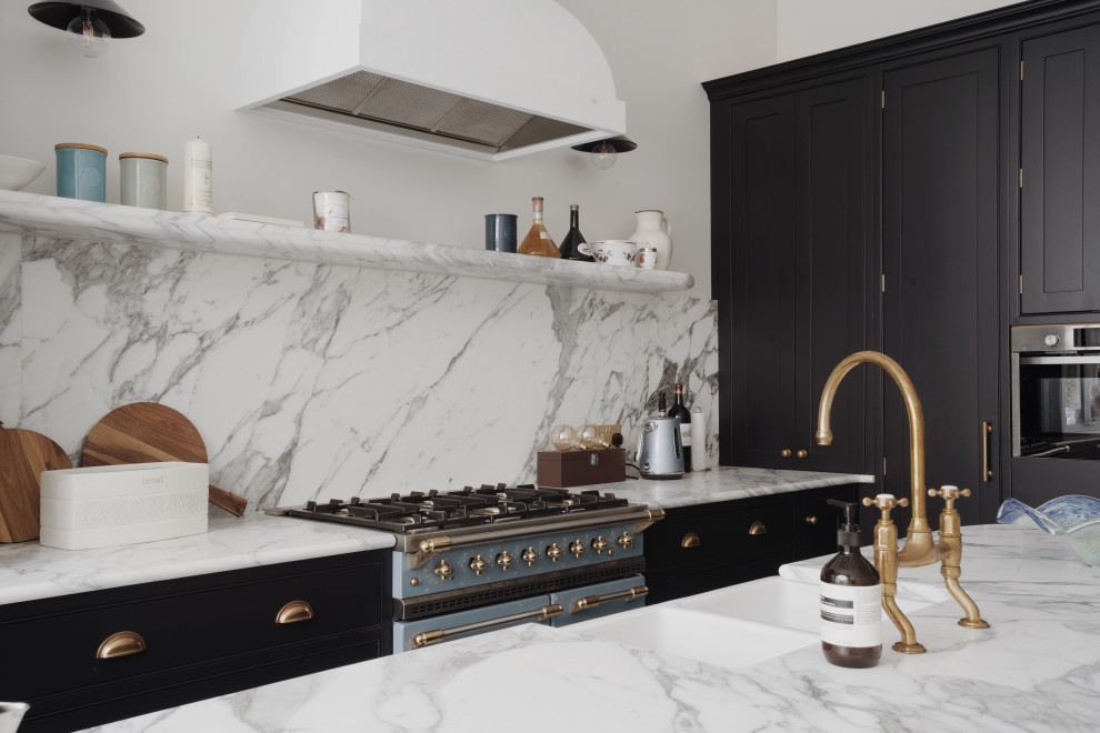 Medium sized traditional galley kitchen/diner in London with a belfast sink, shaker cabinets, black cabinets, marble worktops, white splashback, marble splashback, black appliances, porcelain flooring, an island, blue floors, white worktops, a vaulted ceiling and feature lighting.