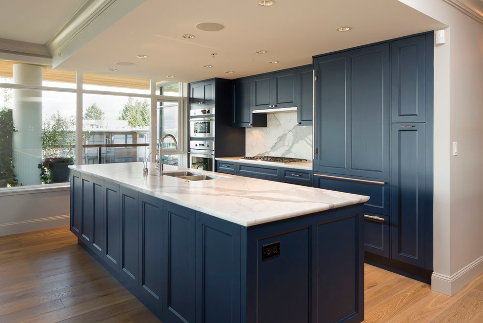 Inspiration for a mid-sized transitional l-shaped open plan kitchen in Vancouver with an undermount sink, recessed-panel cabinets, blue cabinets, marble benchtops, white splashback, marble splashback, stainless steel appliances, medium hardwood floors, with island and brown floor.