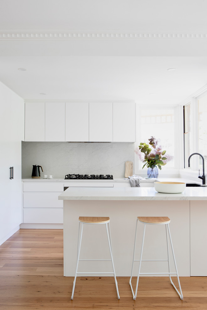 Mid-sized contemporary u-shaped eat-in kitchen in Melbourne with an undermount sink, flat-panel cabinets, white cabinets, quartz benchtops, engineered quartz splashback, black appliances, medium hardwood floors, no island and brown floor.