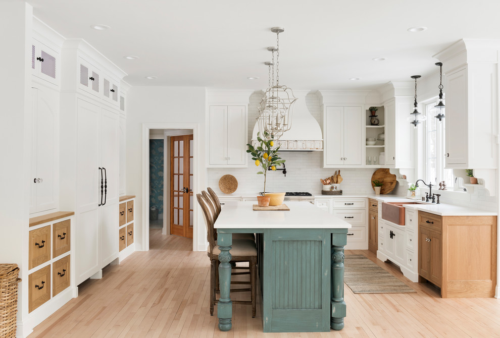 Inspiration for a large country l-shaped eat-in kitchen in Minneapolis with a farmhouse sink, beaded inset cabinets, white cabinets, white splashback, subway tile splashback, stainless steel appliances, light hardwood floors, with island, beige floor and white benchtop.