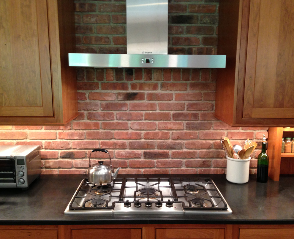 Eat-in kitchen - mid-sized transitional galley gray floor and porcelain tile eat-in kitchen idea in New York with an undermount sink, shaker cabinets, medium tone wood cabinets, granite countertops, stainless steel appliances, red backsplash, brick backsplash, no island and black countertops