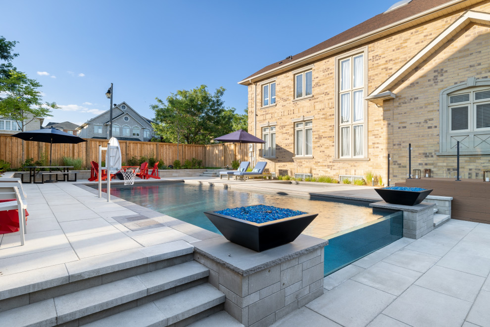 Example of a mid-sized transitional backyard concrete paver and rectangular infinity pool landscaping design in Toronto