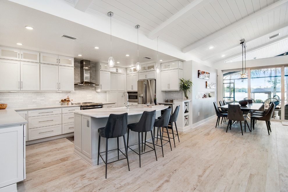 Inspiration for a large beach style u-shaped open plan kitchen in Orlando with an undermount sink, shaker cabinets, white cabinets, quartz benchtops, white splashback, marble splashback, stainless steel appliances, porcelain floors, with island and beige floor.