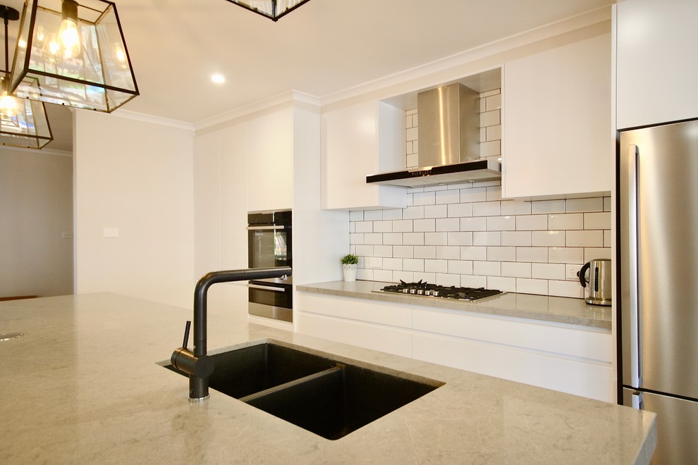 Inspiration for a mid-sized modern single-wall eat-in kitchen in Sydney with an undermount sink, flat-panel cabinets, white cabinets, quartz benchtops, white splashback, ceramic splashback, black appliances, medium hardwood floors, with island and brown floor.