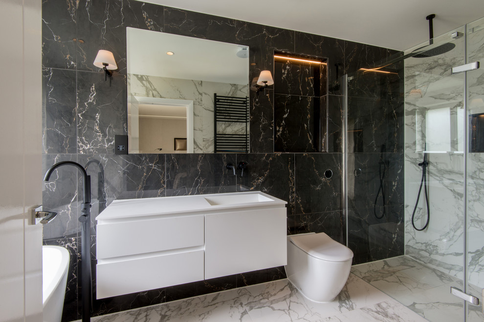 Inspiration for a contemporary bathroom in London with flat-panel cabinets, white cabinets, a freestanding tub, a curbless shower, a one-piece toilet, an integrated sink, white floor, a hinged shower door and white benchtops.