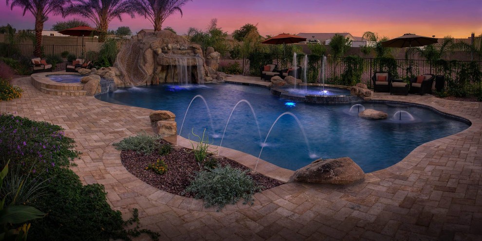 This is an example of a large beach style backyard custom-shaped natural pool in Phoenix with a water slide and natural stone pavers.
