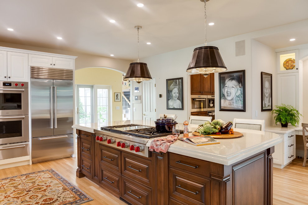 This is an example of a mid-sized traditional l-shaped open plan kitchen in Sacramento with a farmhouse sink, raised-panel cabinets, white cabinets, quartz benchtops, white splashback, porcelain splashback, stainless steel appliances, light hardwood floors, with island, beige floor and beige benchtop.