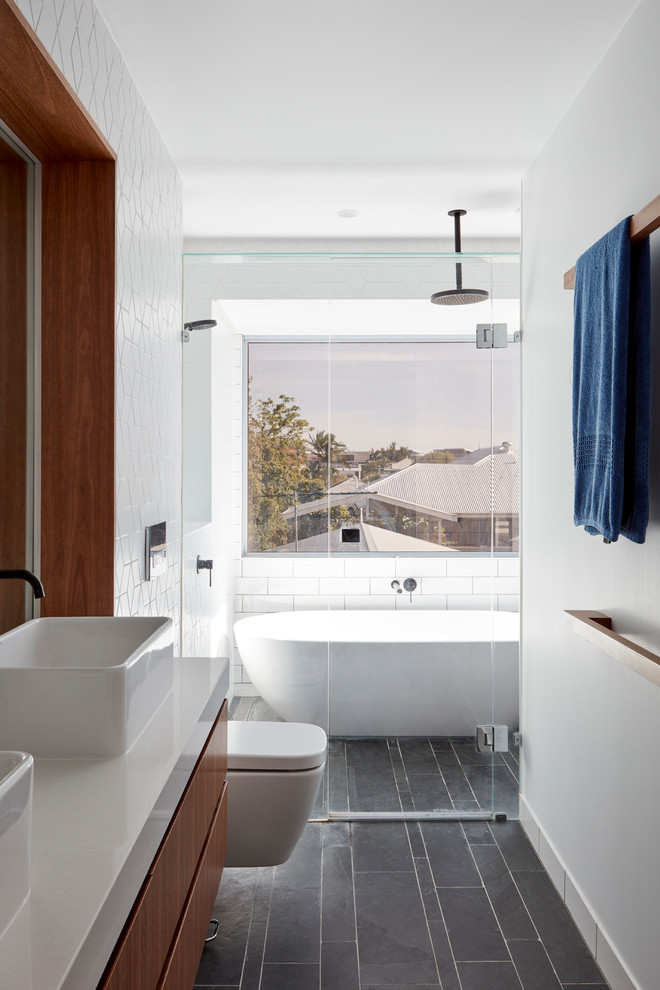 Design ideas for a contemporary master bathroom in Brisbane with flat-panel cabinets, medium wood cabinets, a freestanding tub, an alcove shower, a wall-mount toilet, white tile, white walls, a vessel sink, concrete benchtops, black floor, a hinged shower door and grey benchtops.