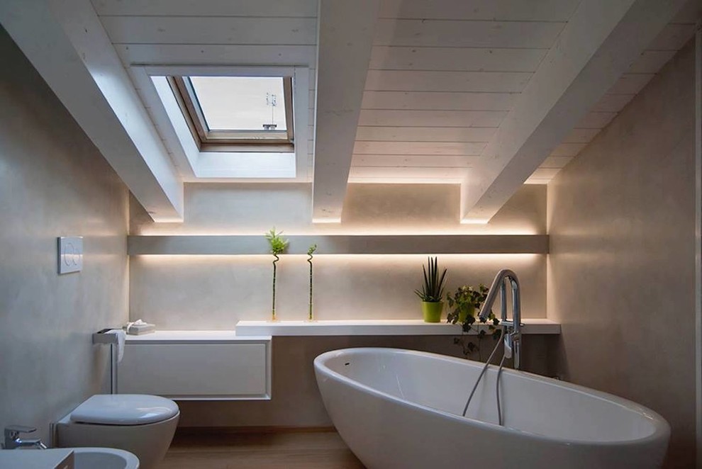 This is an example of a contemporary bathroom in Milan with a freestanding tub, a wall-mount toilet, beige walls, light hardwood floors and beige floor.