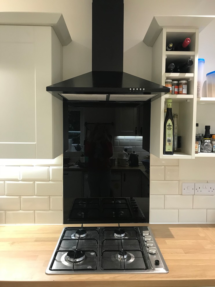 Mid-sized traditional u-shaped separate kitchen in Other with a single-bowl sink, shaker cabinets, white cabinets, laminate benchtops, black splashback, glass sheet splashback, black appliances, vinyl floors, no island and grey floor.