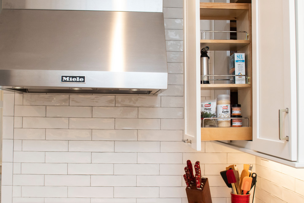 Example of a mid-sized transitional l-shaped medium tone wood floor and brown floor kitchen pantry design in Providence with an undermount sink, recessed-panel cabinets, white cabinets, quartzite countertops, white backsplash, ceramic backsplash, stainless steel appliances, no island and white countertops