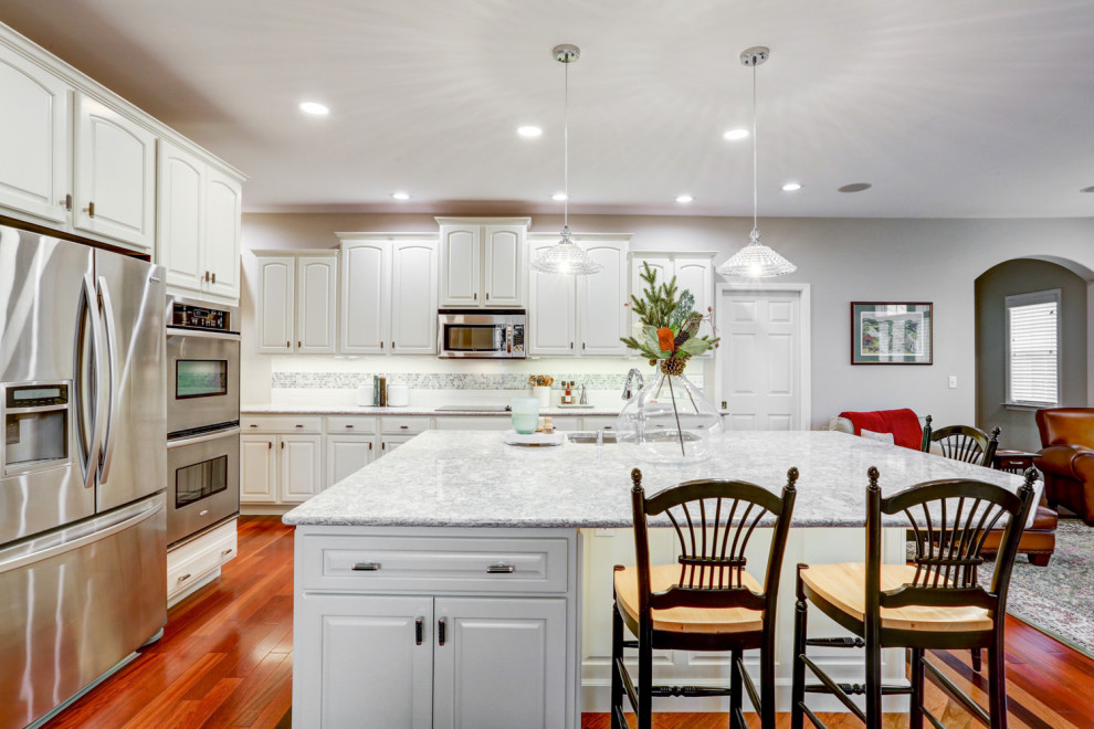 他の地域にある高級な広いトラディショナルスタイルのおしゃれなキッチン (アンダーカウンターシンク、レイズドパネル扉のキャビネット、白いキャビネット、クオーツストーンカウンター、白いキッチンパネル、セラミックタイルのキッチンパネル、シルバーの調理設備、無垢フローリング、茶色い床、白いキッチンカウンター) の写真