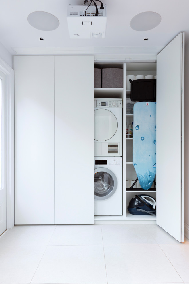 Photo of a medium sized contemporary utility room in London with a single-bowl sink, flat-panel cabinets, white cabinets, composite countertops, ceramic flooring, a stacked washer and dryer, beige floors and white worktops.