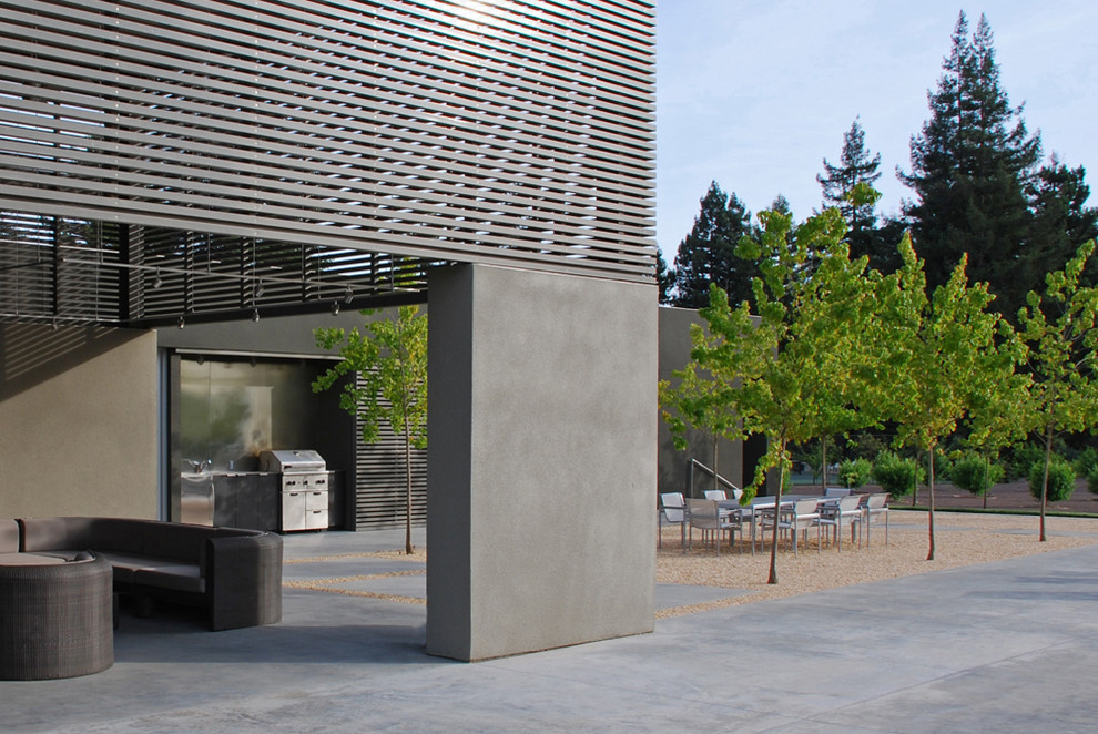 This is an example of an expansive modern backyard patio in San Francisco with an outdoor kitchen, gravel and a roof extension.