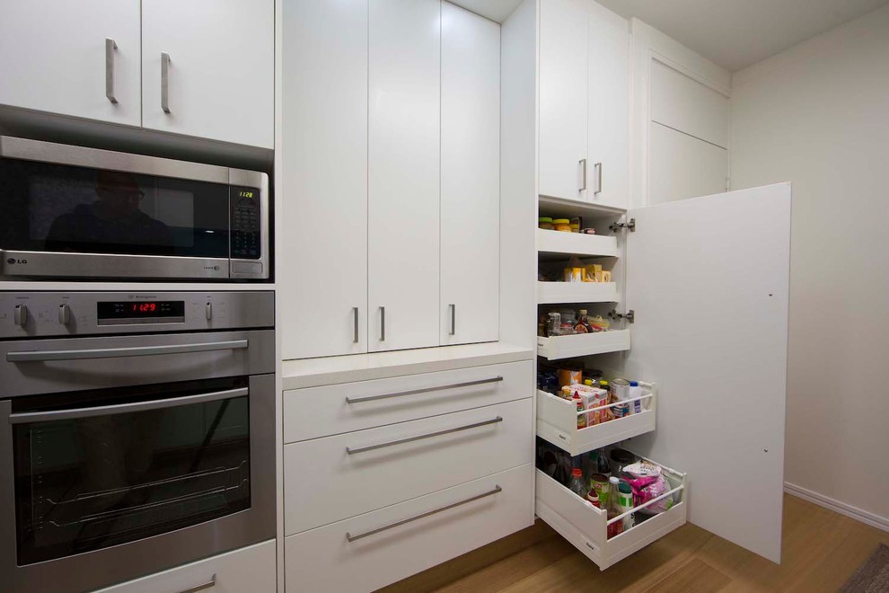 This is an example of a mid-sized contemporary galley kitchen pantry in Sydney with a drop-in sink, flat-panel cabinets, white cabinets, quartz benchtops, blue splashback, stainless steel appliances, medium hardwood floors, no island and white benchtop.