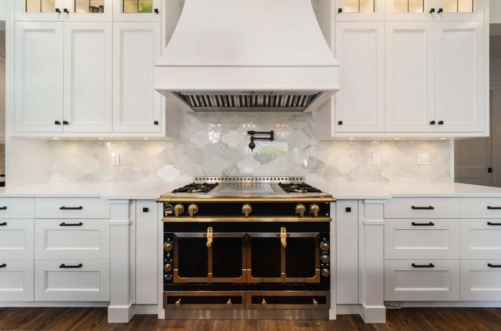 Inspiration for a large arts and crafts open plan kitchen in Vancouver with a farmhouse sink, shaker cabinets, white cabinets, quartz benchtops, white splashback, porcelain splashback, black appliances, dark hardwood floors, with island, brown floor, white benchtop and timber.