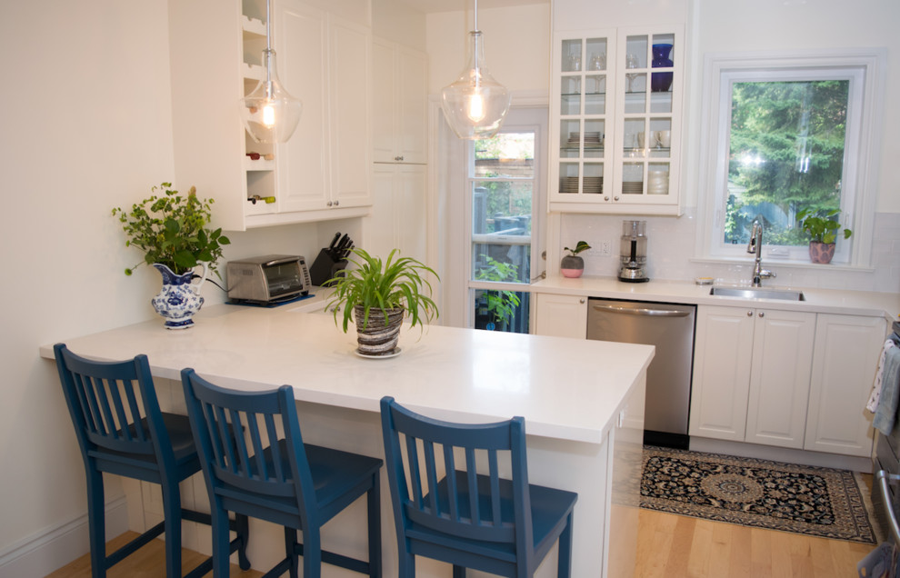 Example of a mid-sized transitional u-shaped light wood floor and brown floor open concept kitchen design in Toronto with an undermount sink, raised-panel cabinets, white cabinets, solid surface countertops, white backsplash, subway tile backsplash, stainless steel appliances, no island and white countertops