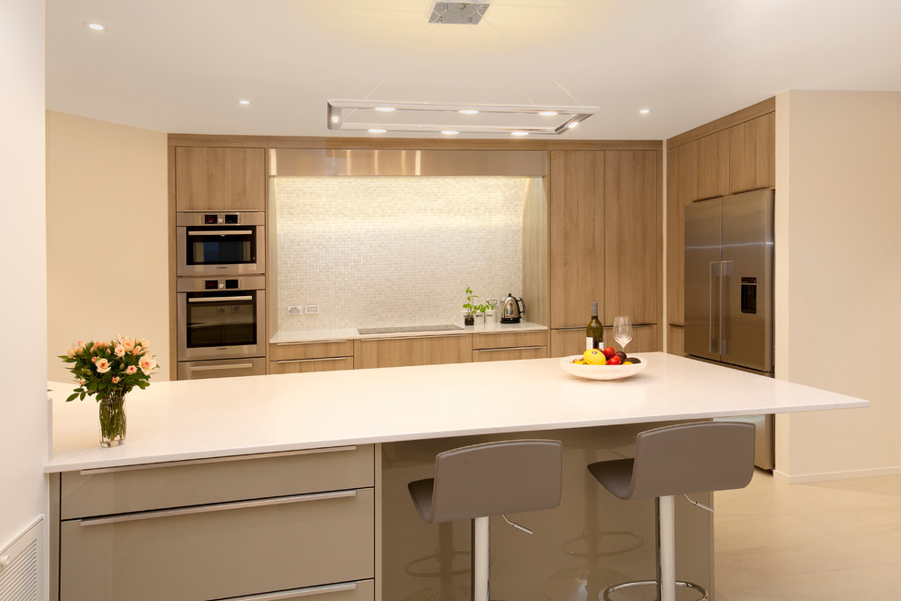 This is an example of a mid-sized contemporary galley eat-in kitchen in Christchurch with light wood cabinets, white splashback, mosaic tile splashback, stainless steel appliances, with island, quartz benchtops, white benchtop, an undermount sink, ceramic floors and beige floor.