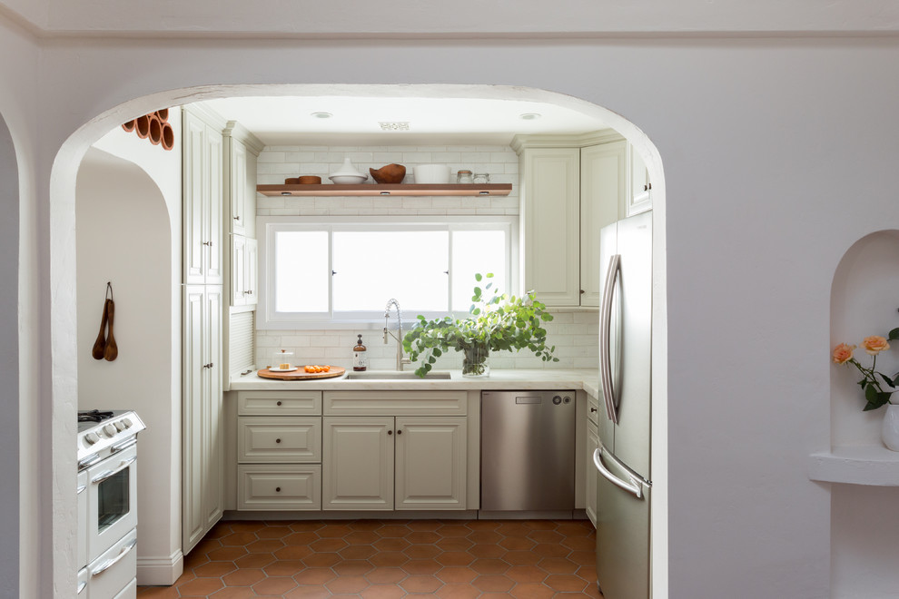 Design ideas for a mediterranean kitchen in Los Angeles with a drop-in sink, beige cabinets, white splashback, brick splashback, stainless steel appliances and terra-cotta floors.