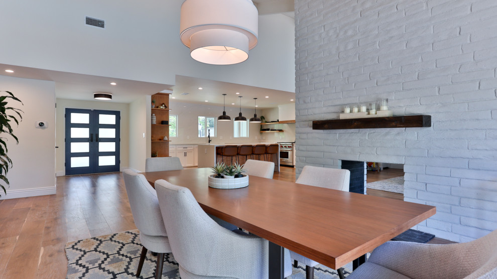 Cette photo montre une grande salle à manger ouverte sur la cuisine tendance avec un mur blanc, un sol en bois brun, une cheminée double-face, un manteau de cheminée en brique, un sol marron et un plafond en lambris de bois.