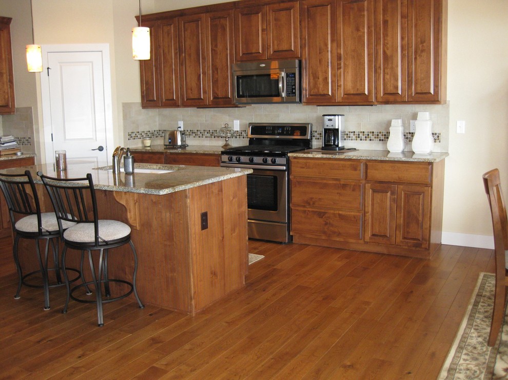 Open concept kitchen - mid-sized transitional galley medium tone wood floor open concept kitchen idea with an undermount sink, raised-panel cabinets, medium tone wood cabinets, granite countertops, multicolored backsplash, ceramic backsplash, stainless steel appliances and an island