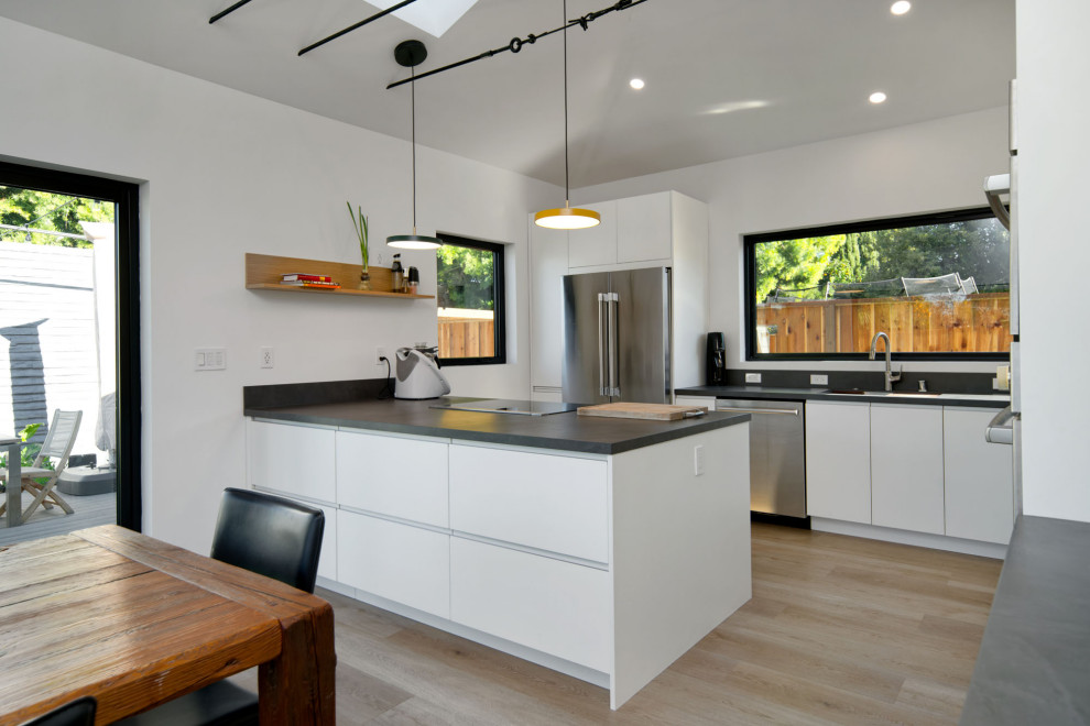 Inspiration for a contemporary l-shaped kitchen in San Francisco with a submerged sink, flat-panel cabinets, white cabinets, composite countertops, grey splashback, medium hardwood flooring, an island, grey worktops and a vaulted ceiling.