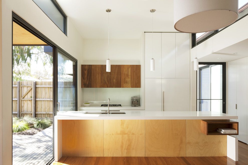 Design ideas for a mid-sized modern galley eat-in kitchen in Melbourne with an undermount sink, flat-panel cabinets, white cabinets, quartz benchtops, white splashback, glass sheet splashback, stainless steel appliances, with island and medium hardwood floors.