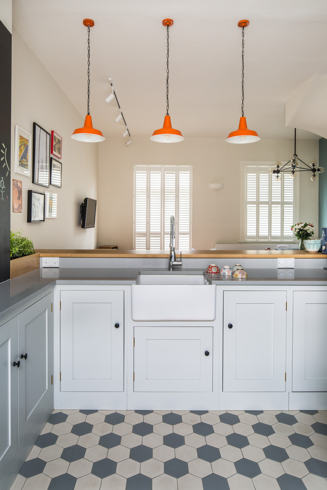 Small contemporary l-shaped open plan kitchen in London with a farmhouse sink, shaker cabinets, white cabinets, quartz benchtops, blue splashback, subway tile splashback, stainless steel appliances, ceramic floors, a peninsula and multi-coloured floor.
