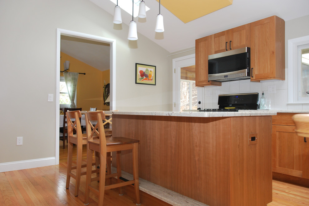 Example of a large transitional l-shaped medium tone wood floor enclosed kitchen design in Boston with an undermount sink, shaker cabinets, medium tone wood cabinets, granite countertops, white backsplash, ceramic backsplash, stainless steel appliances and an island