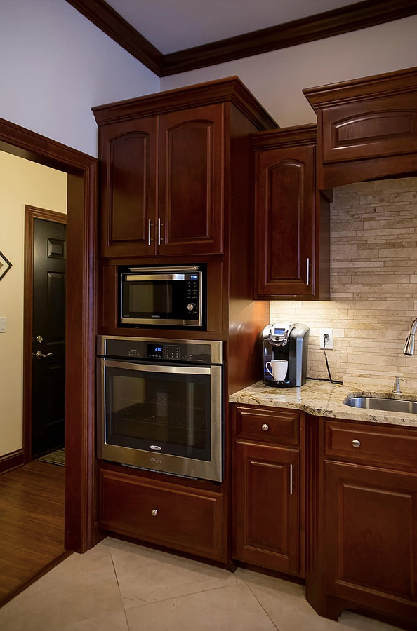 Large minimalist u-shaped porcelain tile and beige floor open concept kitchen photo with an undermount sink, raised-panel cabinets, dark wood cabinets, granite countertops, beige backsplash, matchstick tile backsplash, stainless steel appliances, an island and multicolored countertops