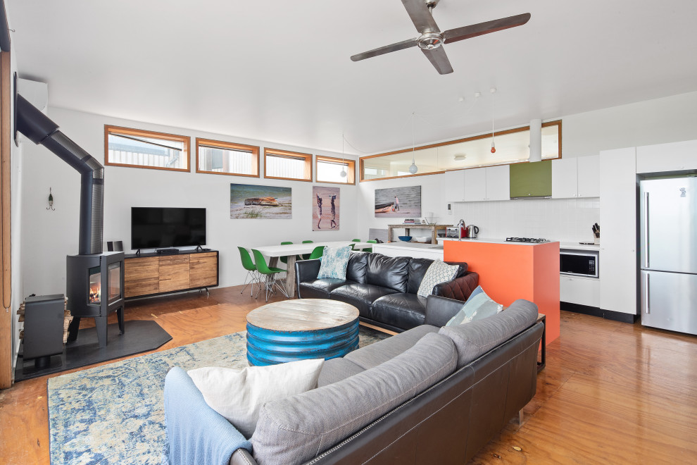 Immagine di un soggiorno minimal di medie dimensioni con pareti bianche, pavimento in compensato e stufa a legna