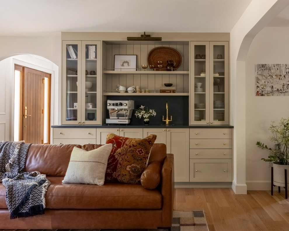 Mid-sized elegant single-wall light wood floor wet bar photo in Seattle with an undermount sink, glass-front cabinets, beige cabinets, quartzite countertops, black backsplash, stone slab backsplash and black countertops