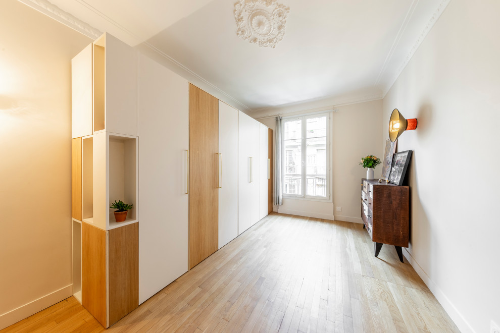 Mid-sized contemporary gender-neutral built-in wardrobe in Paris with beaded inset cabinets, light wood cabinets, light hardwood floors and beige floor.