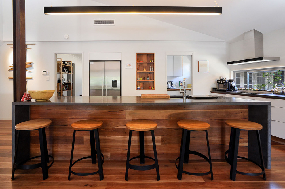 Photo of a mid-sized modern kitchen in Townsville with a double-bowl sink, white cabinets, concrete benchtops, stainless steel appliances, medium hardwood floors, with island, brown floor and black benchtop.