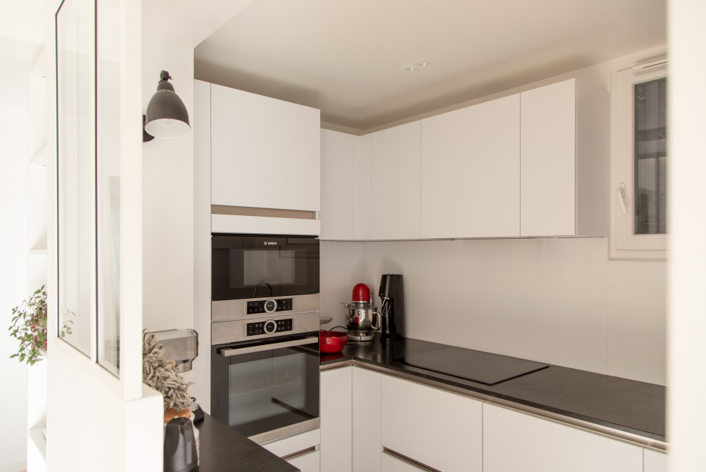 Photo of a small modern u-shaped eat-in kitchen in Paris with an undermount sink, flat-panel cabinets, white cabinets, quartz benchtops, white splashback, glass sheet splashback, black appliances, marble floors, no island, black floor and black benchtop.
