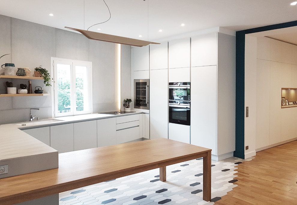 Photo of a scandinavian u-shaped kitchen in Paris with an undermount sink, flat-panel cabinets, white cabinets, black appliances, a peninsula, grey floor and grey benchtop.