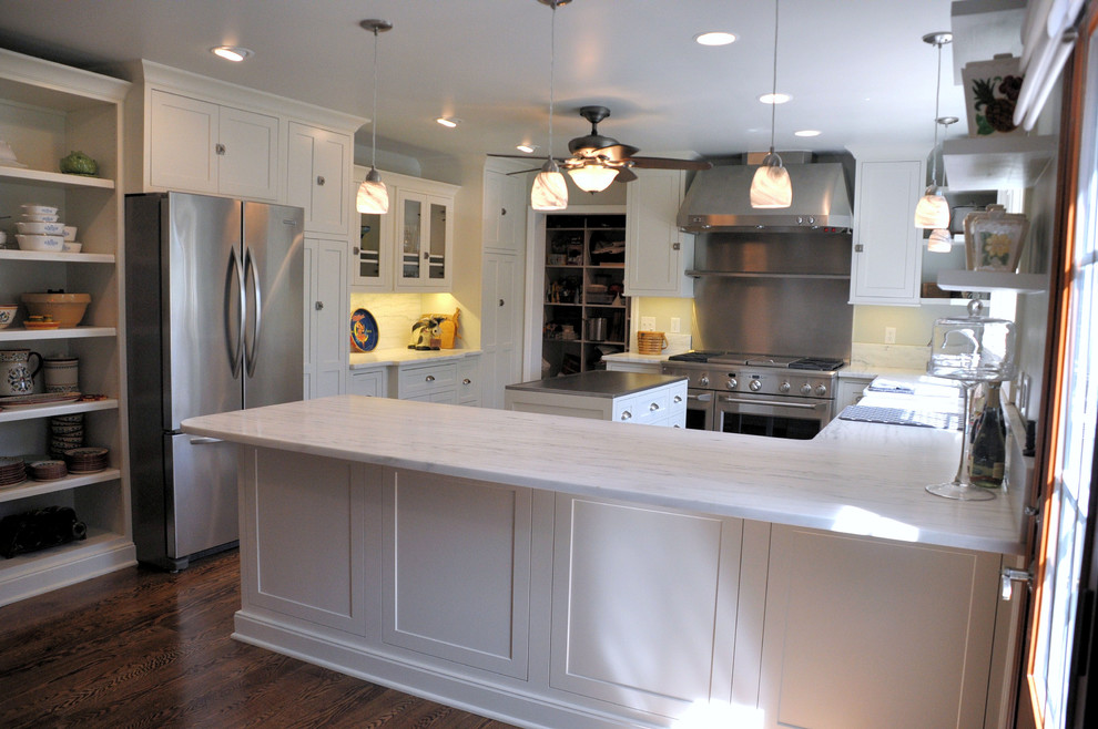This is an example of a mid-sized transitional u-shaped kitchen in St Louis with a farmhouse sink, white cabinets, quartzite benchtops, white splashback, stainless steel appliances, dark hardwood floors, with island and shaker cabinets.