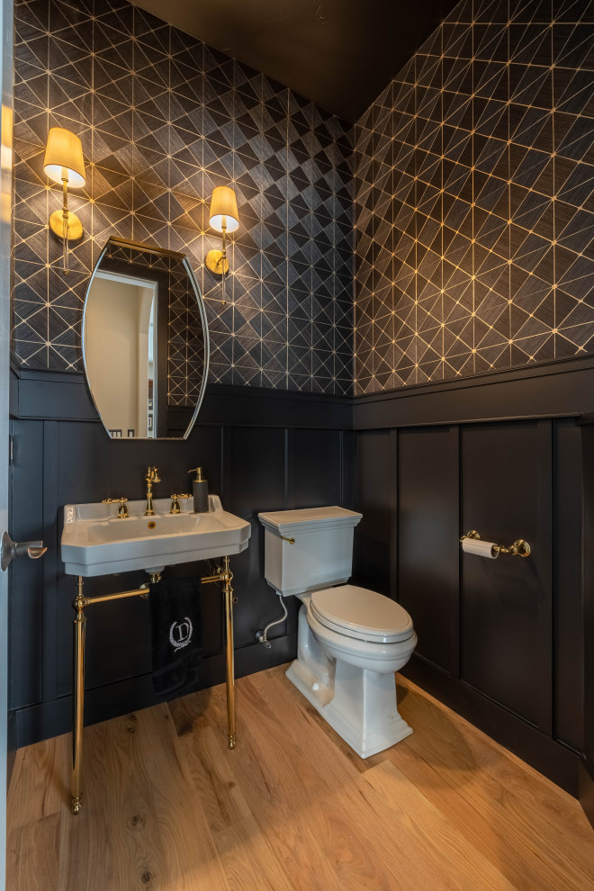 Design ideas for a small powder room in Denver with white cabinets, a one-piece toilet, black walls, light hardwood floors, an integrated sink, a freestanding vanity, wallpaper and decorative wall panelling.