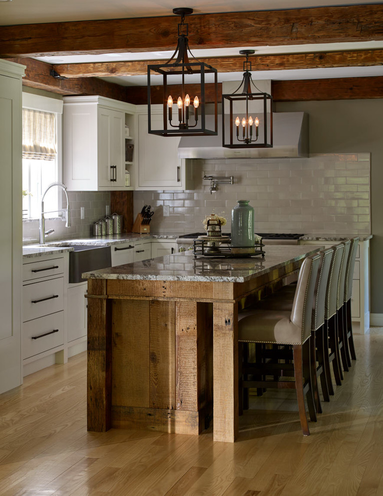 Inspiration for a large country l-shaped eat-in kitchen in Portland Maine with a farmhouse sink, shaker cabinets, white cabinets, granite benchtops, grey splashback, subway tile splashback, panelled appliances, light hardwood floors, with island, multi-coloured benchtop, beige floor and exposed beam.