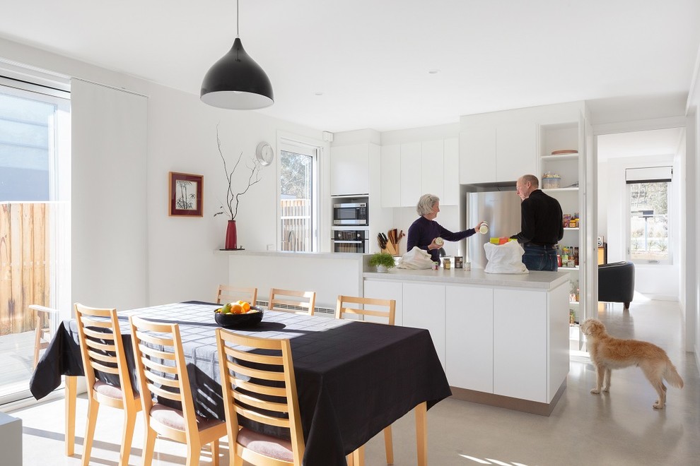Photo of a contemporary galley eat-in kitchen in Canberra - Queanbeyan with flat-panel cabinets, white cabinets, stainless steel appliances, concrete floors and a peninsula.