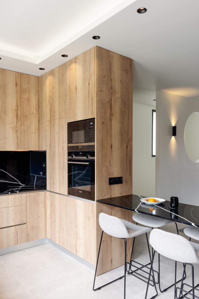 パリにある高級な広いコンテンポラリースタイルのおしゃれなキッチン (アンダーカウンターシンク、フラットパネル扉のキャビネット、黒いキャビネット、木材カウンター、黒いキッチンパネル、大理石のキッチンパネル、黒い調理設備、セラミックタイルの床、グレーの床、ベージュのキッチンカウンター) の写真