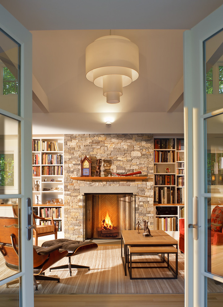 This is an example of a midcentury living room in Boston with a library and a stone fireplace surround.