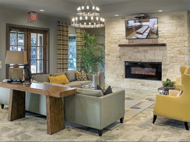 This is an example of a mid-sized contemporary open concept family room in Austin with a game room, grey walls, ceramic floors, a ribbon fireplace, a stone fireplace surround, a wall-mounted tv and brown floor.