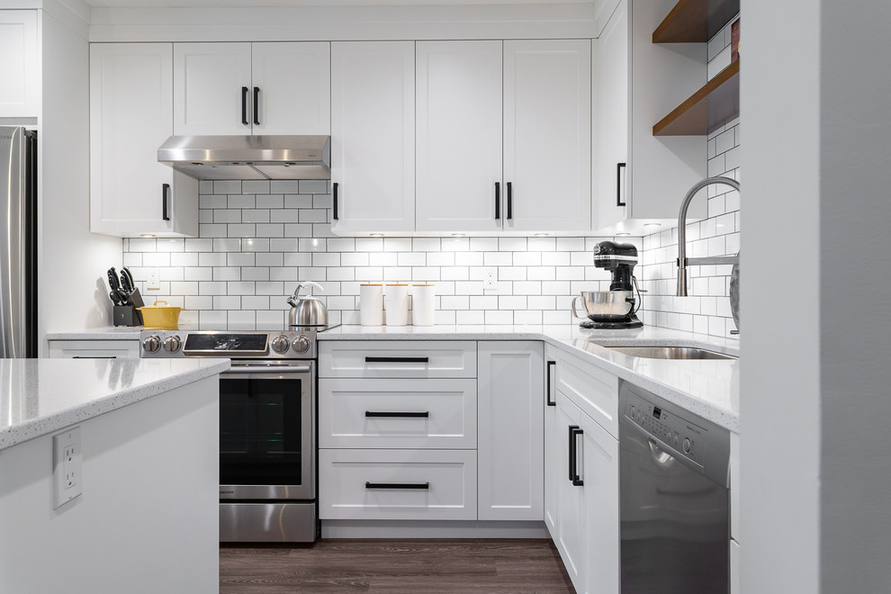 Inspiration for a mid-sized transitional l-shaped eat-in kitchen in Vancouver with an undermount sink, white cabinets, quartz benchtops, white splashback, subway tile splashback, stainless steel appliances, with island, brown floor, white benchtop, shaker cabinets and vinyl floors.