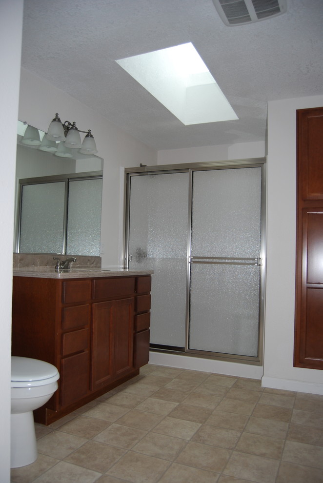 Small traditional 3/4 bathroom in Portland with recessed-panel cabinets, dark wood cabinets, an alcove shower, a two-piece toilet, beige walls, vinyl floors, an undermount sink and solid surface benchtops.