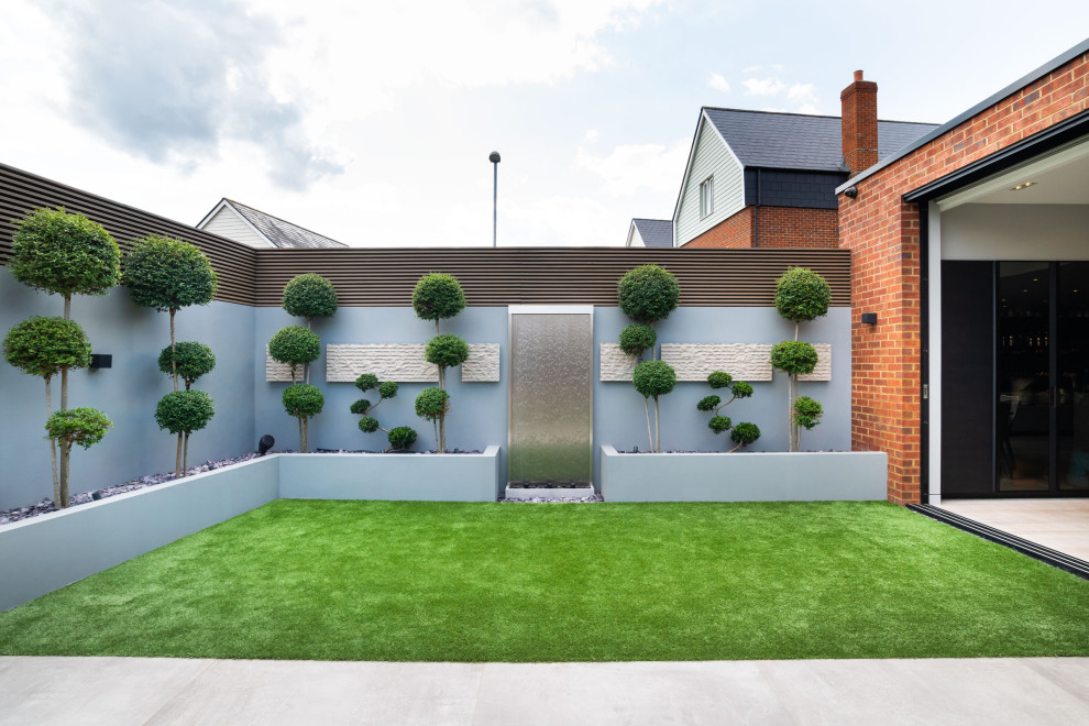 This is an example of a large contemporary backyard full sun formal garden for summer in London with with waterfall and natural stone pavers.
