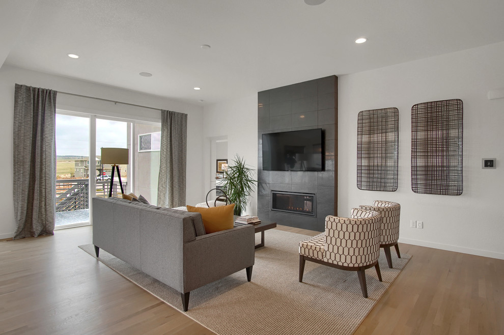 Inspiration for an expansive midcentury open concept living room in Denver with white walls, light hardwood floors, a standard fireplace, a tile fireplace surround, a wall-mounted tv and beige floor.