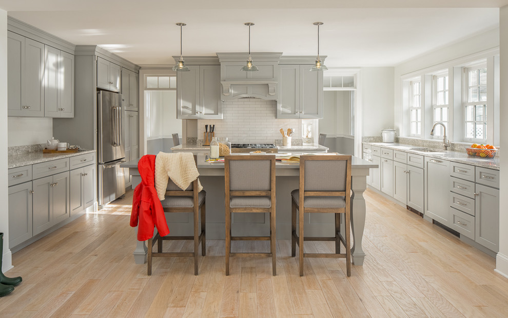 Transitional u-shaped kitchen in Portland Maine with an undermount sink, shaker cabinets, grey cabinets, stainless steel appliances, light hardwood floors, with island, beige floor and grey benchtop.