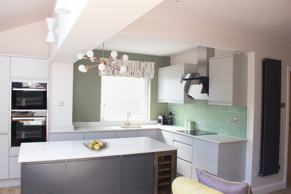 Inspiration for a mid-sized midcentury l-shaped eat-in kitchen in Cardiff with an undermount sink, flat-panel cabinets, grey cabinets, solid surface benchtops, green splashback, cement tile splashback, black appliances, vinyl floors, with island, beige floor and white benchtop.