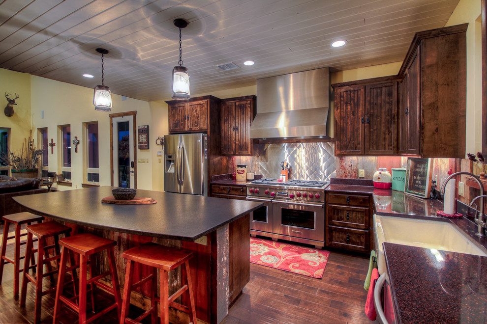 Inspiration for a mid-sized country l-shaped eat-in kitchen in Austin with a farmhouse sink, beaded inset cabinets, dark wood cabinets, granite benchtops, metallic splashback, metal splashback, stainless steel appliances, dark hardwood floors, with island and brown floor.